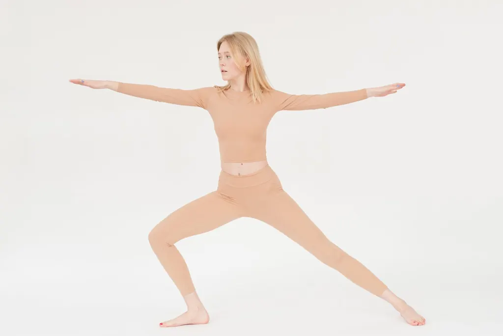 Woman in a warrior yoga pose against a soft neutral backdrop